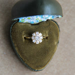 Diamond ring in a heart-shaped green jewelry box with floral interior on a beige surface