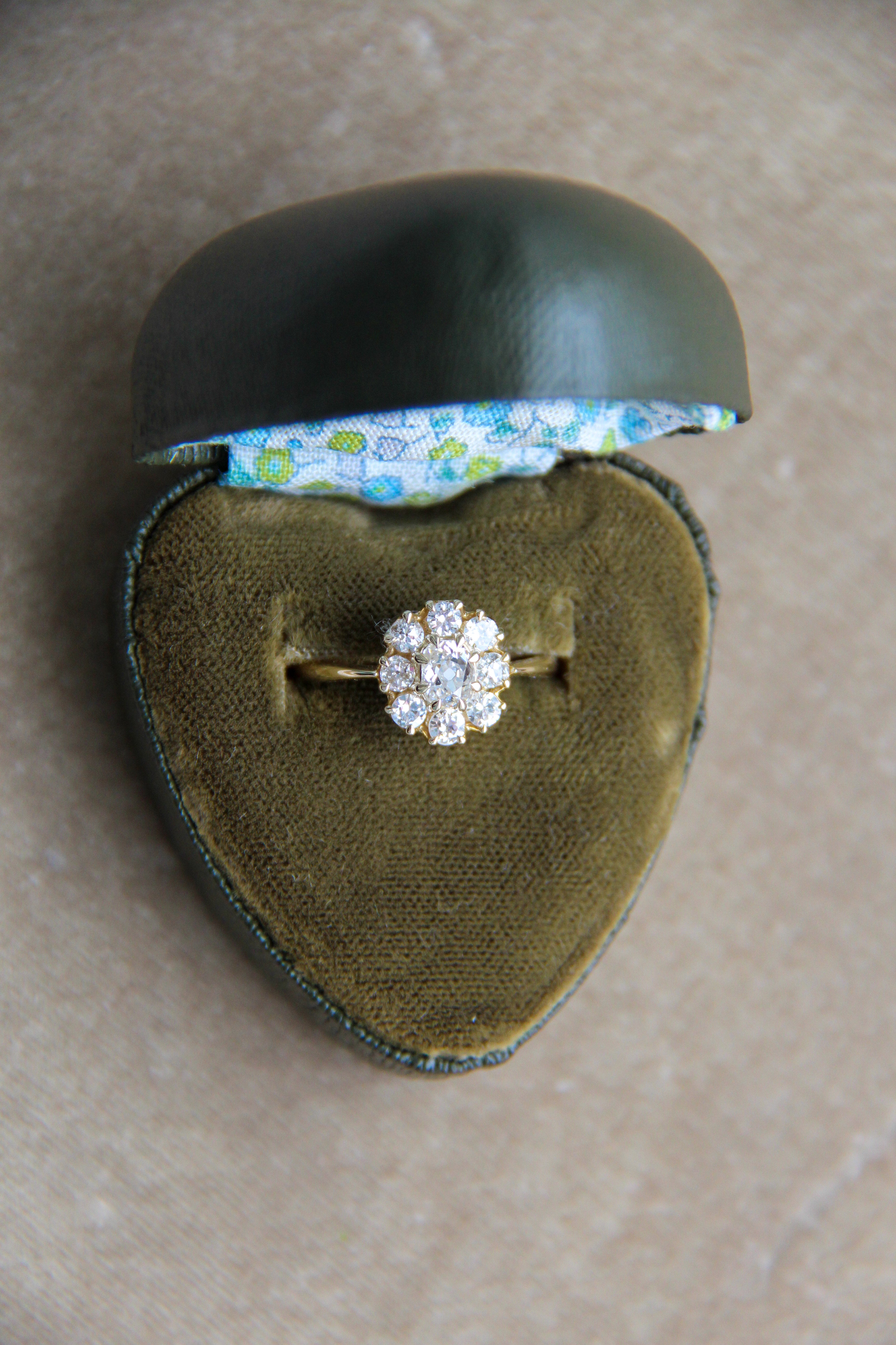 Diamond ring in a heart-shaped green jewelry box with floral interior on a beige surface