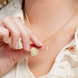 Close-up of a person holding a gold charm with a necklace around their neck.