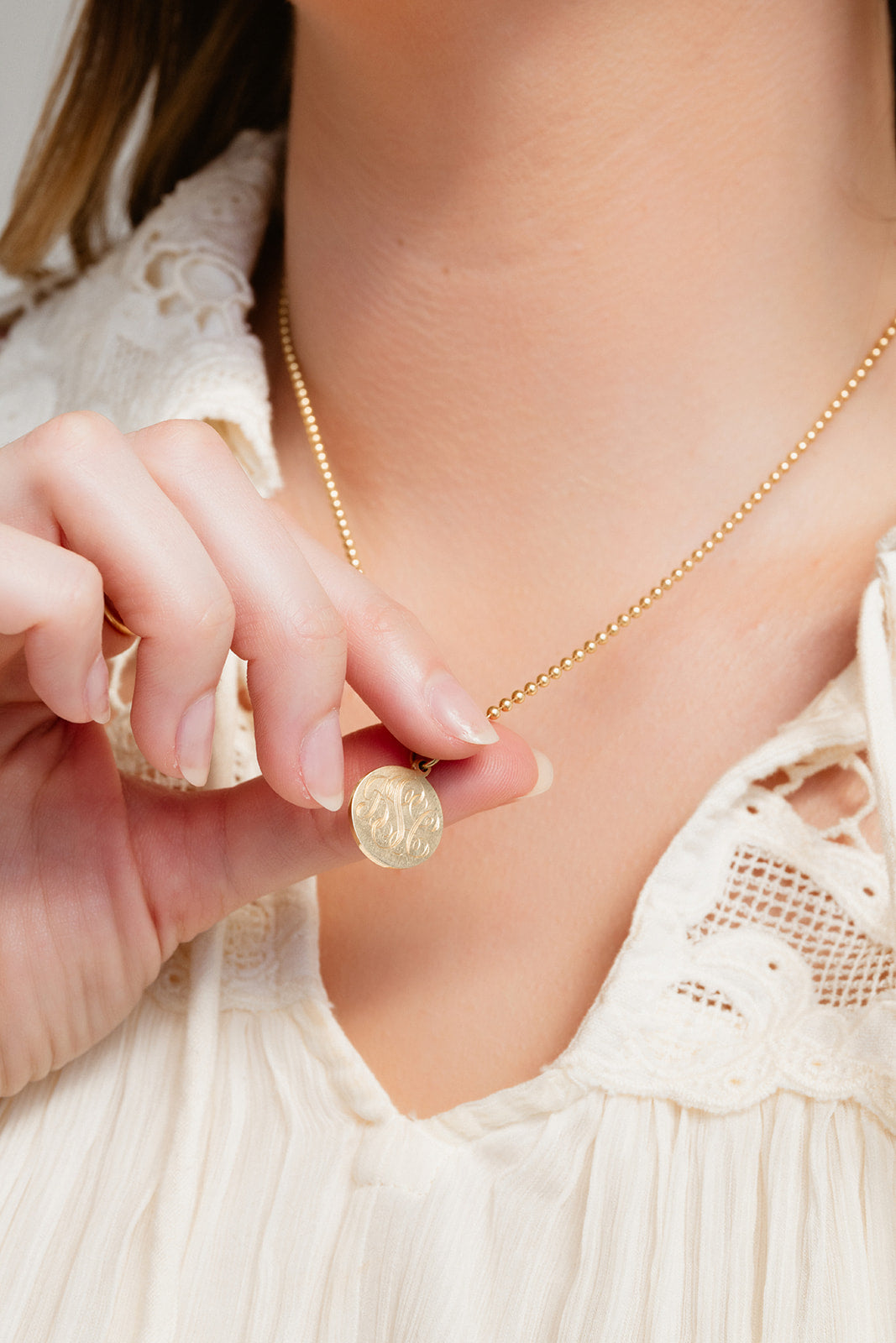 Close-up of a person holding a gold charm with a necklace around their neck.