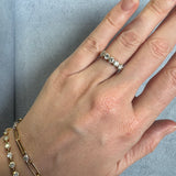 Hand wearing a diamond ring and gold bracelet on a gray surface