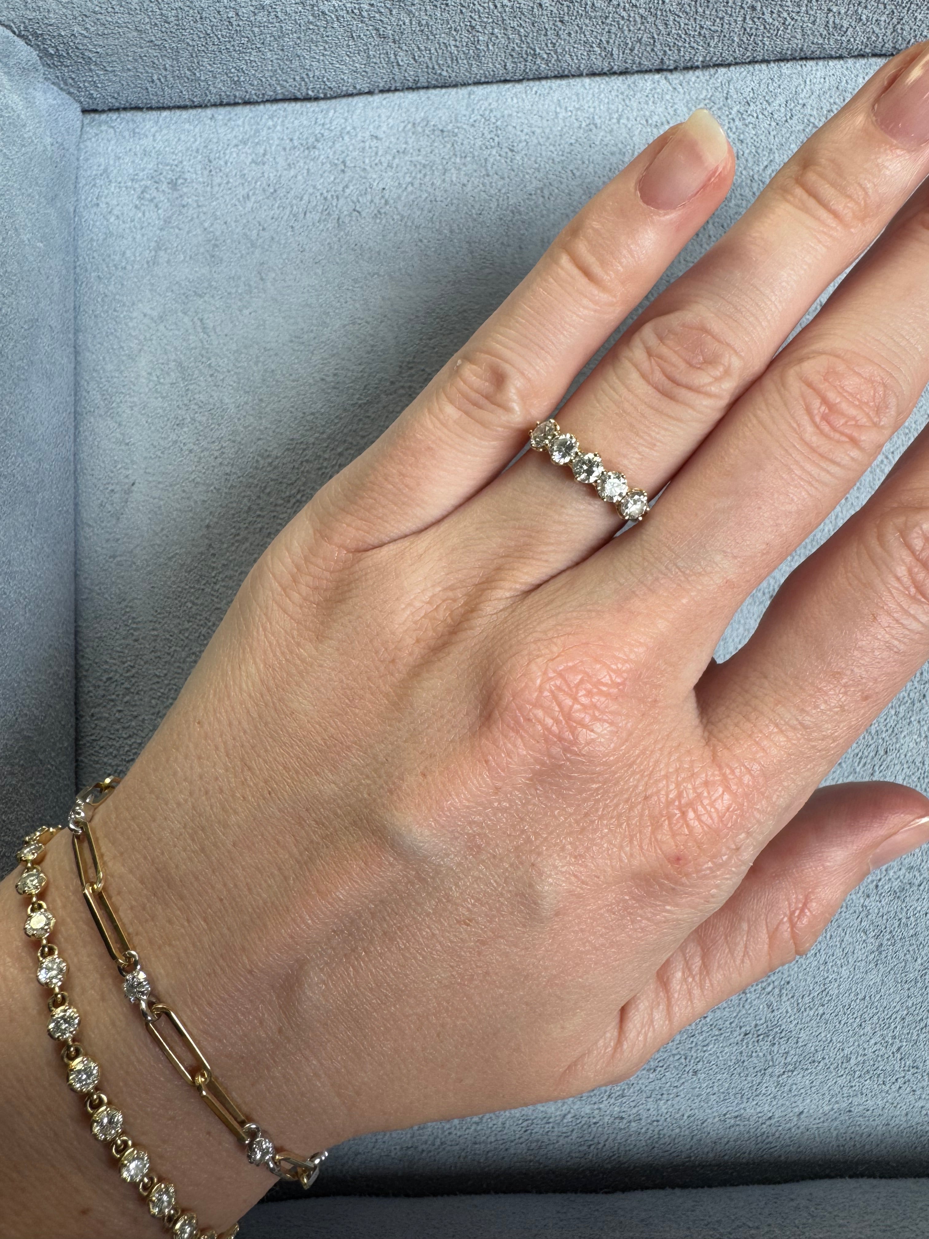 Hand wearing a diamond ring and gold bracelet on a gray surface