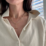 Person wearing a cream-colored shirt with layered gold necklaces