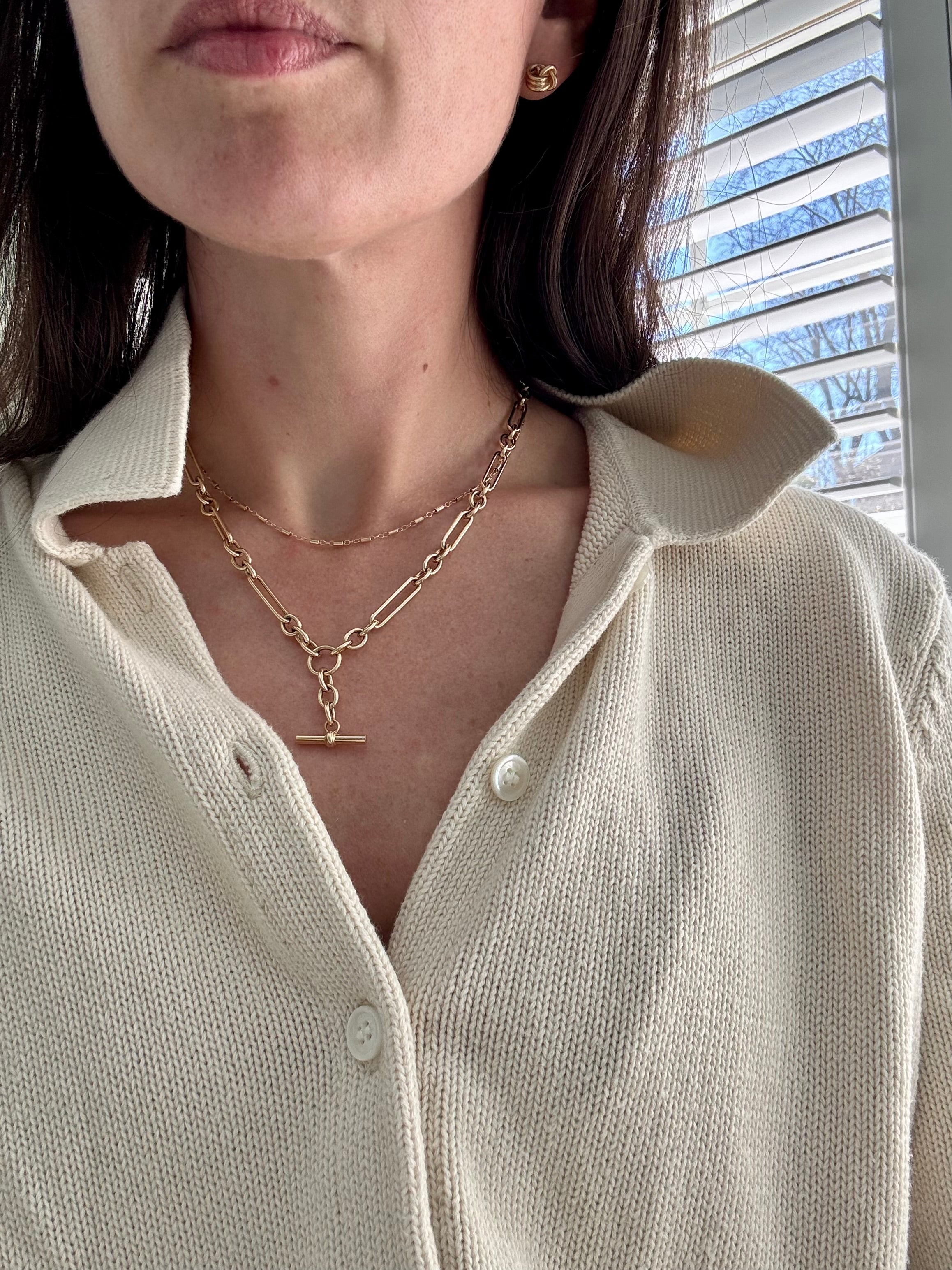 Person wearing a cream-colored shirt with layered gold necklaces
