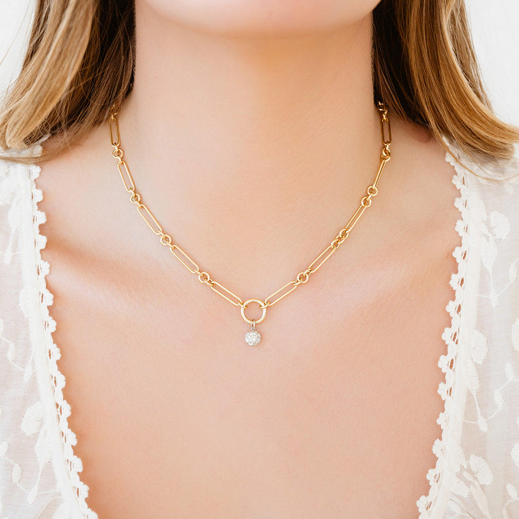 Gold necklace with a diamond pendant worn by a person against a white background