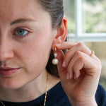 Woman wearing a pearl earring and adjusting it with her hand.
