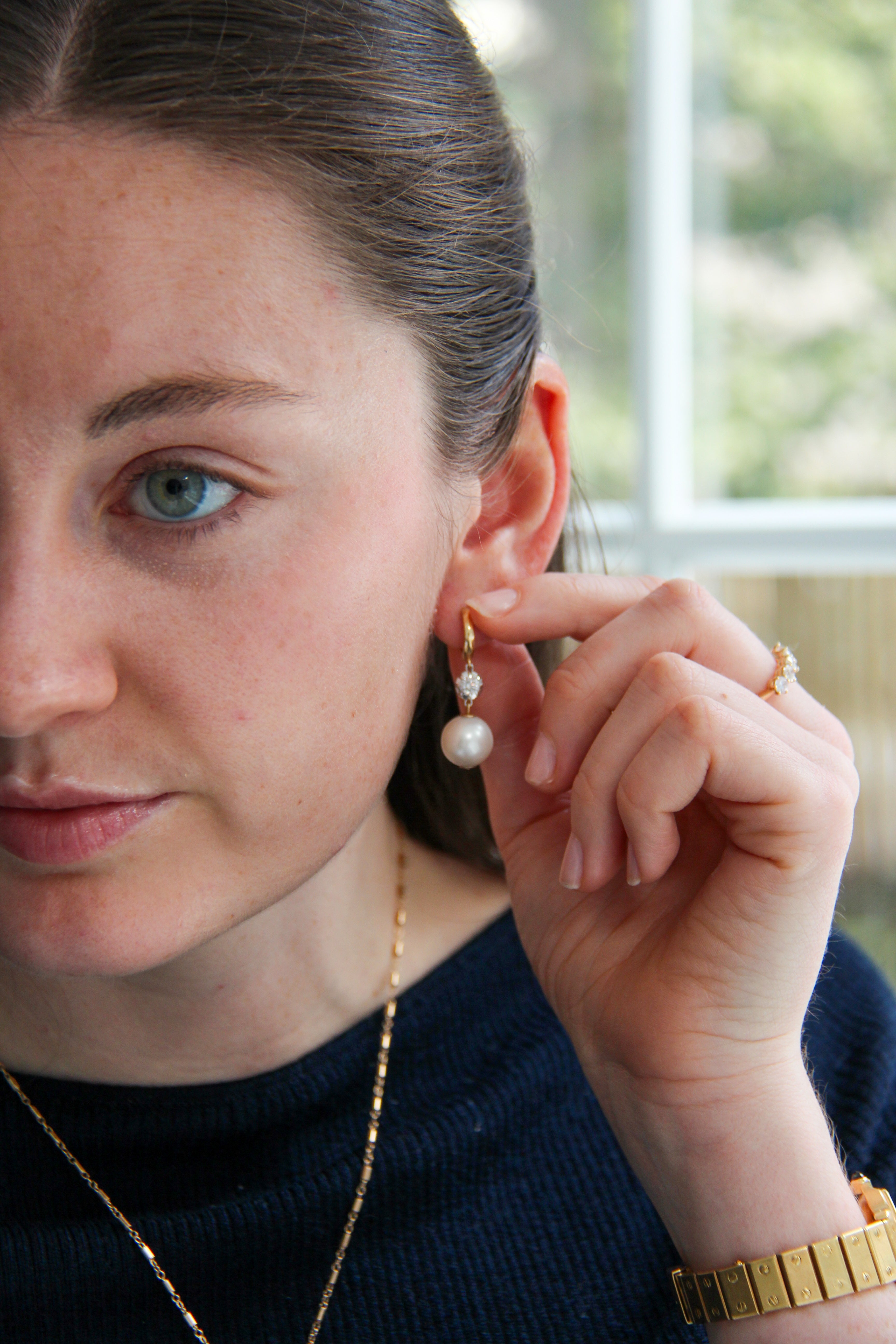 Woman wearing a pearl earring and adjusting it with her hand.