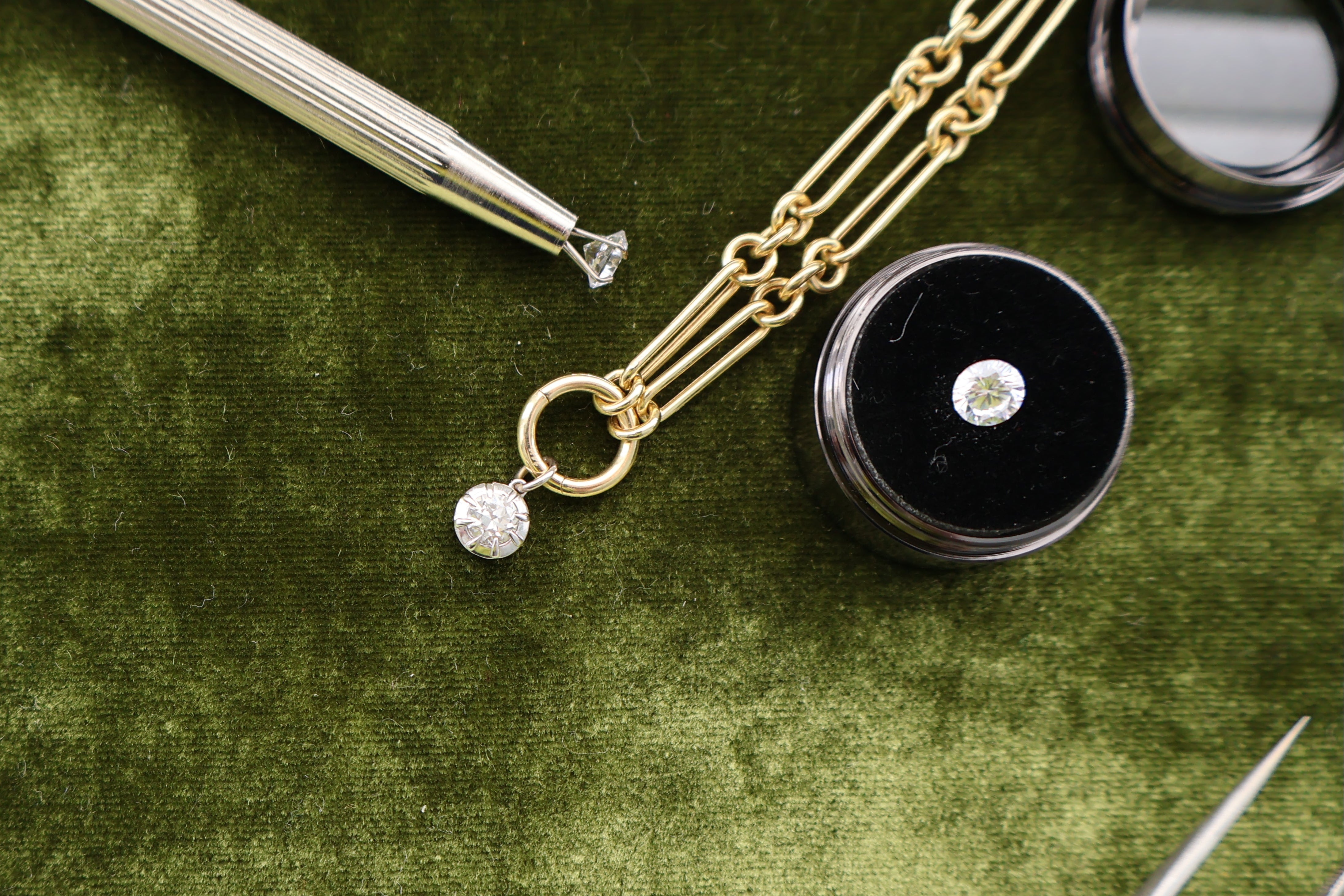 Jewelry set with gold chain, black container, and tools on a green surface with La Prairie logo.