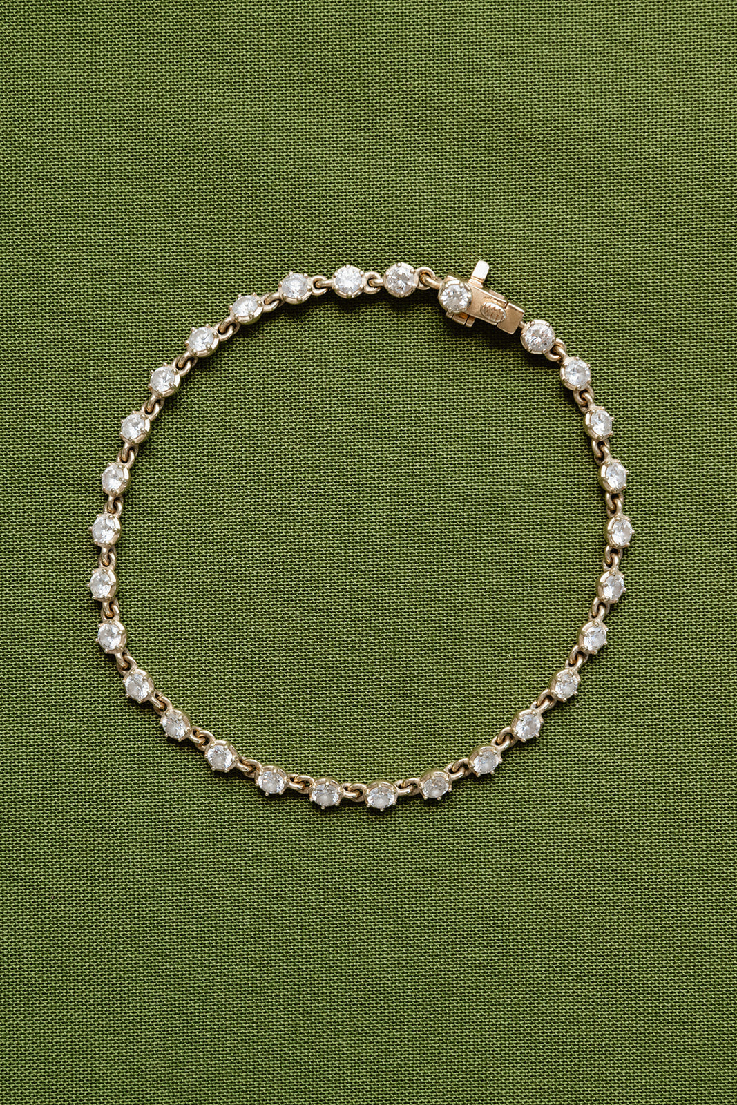 Gold bracelet with clear stones on a green fabric background
