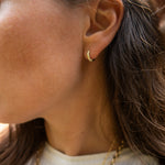 A close-up side profile of a woman wearing a small gold hoop earring