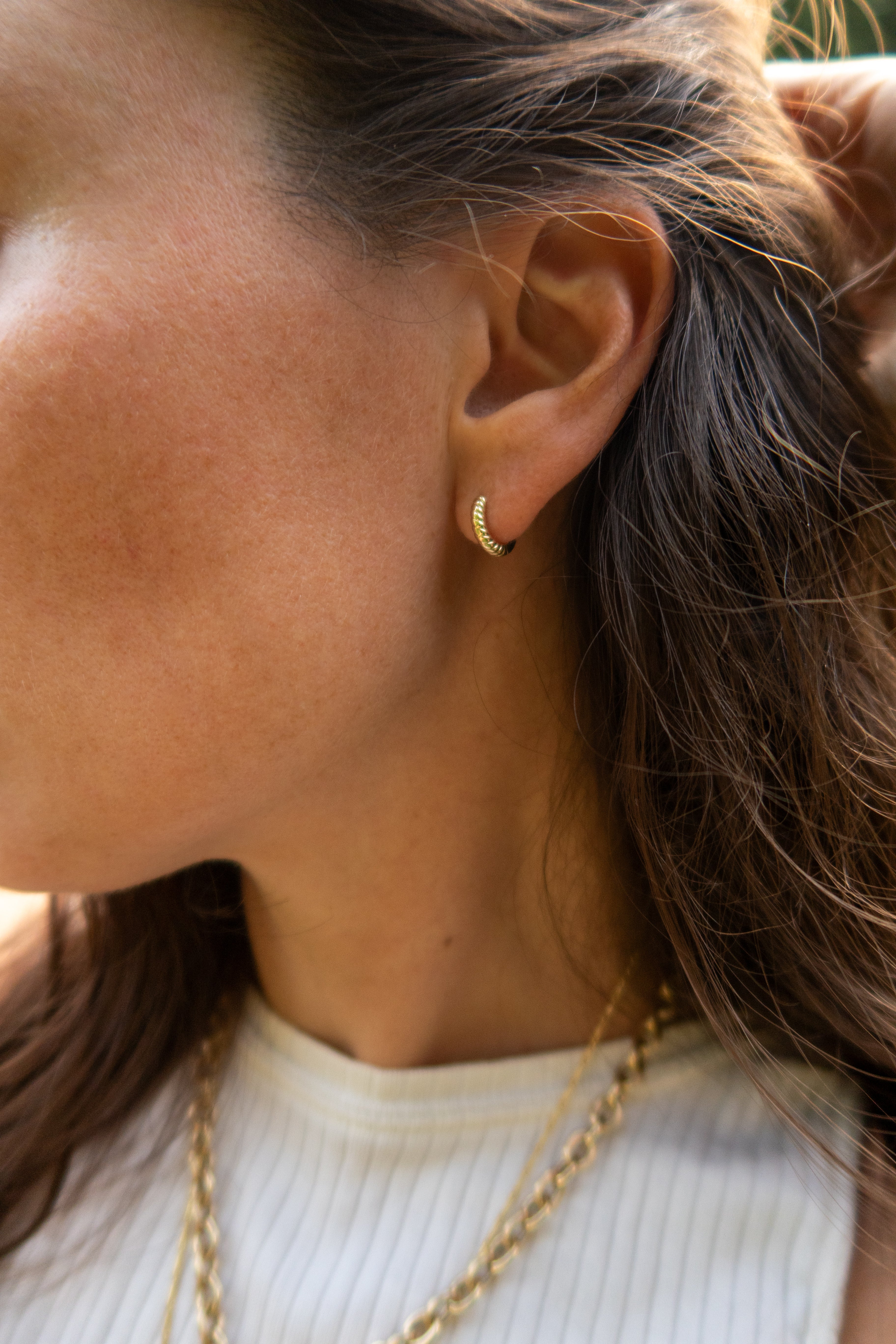 A close-up side profile of a woman wearing a small gold hoop earring