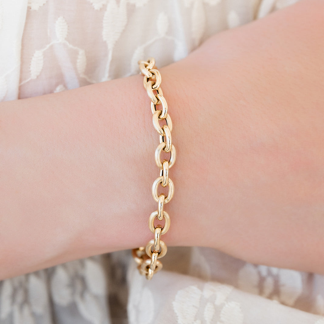 Gold chain bracelet on a wrist with a light background