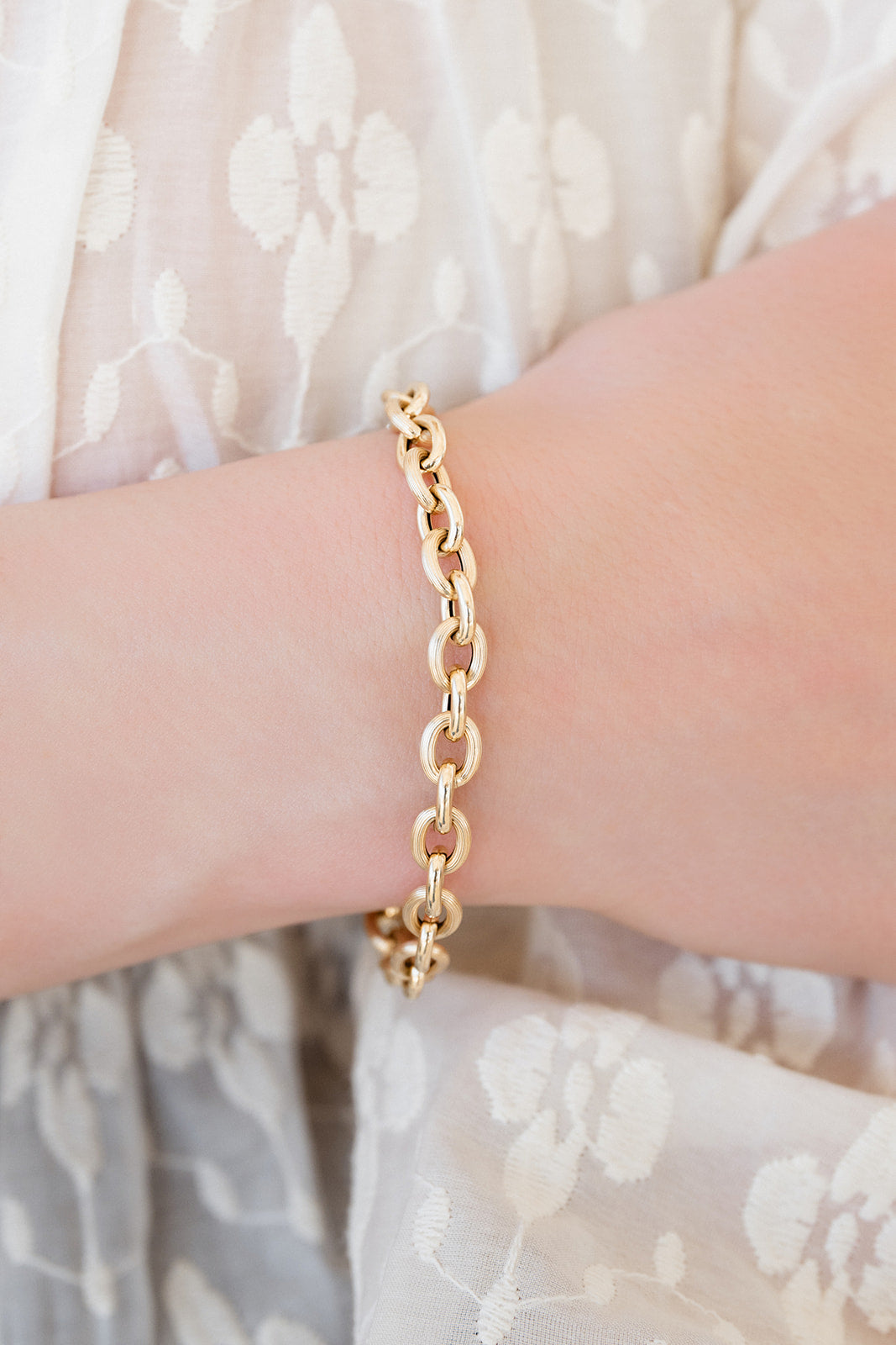 Gold chain bracelet on a wrist with a light background