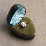 Diamond ring in a heart-shaped green velvet box with floral interior on a beige background