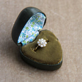 Diamond ring in a heart-shaped green velvet box with floral interior on a beige background