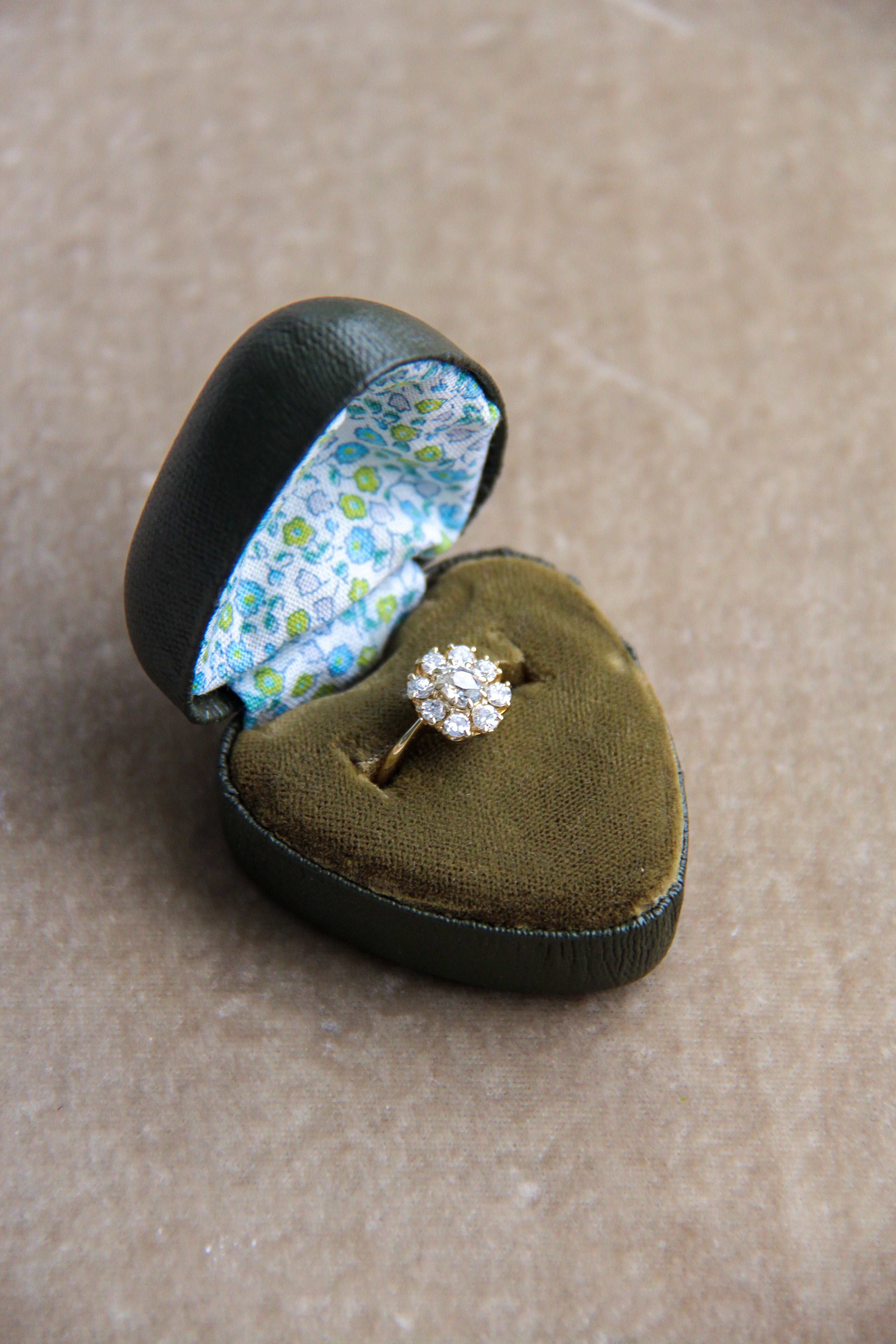 Diamond ring in a heart-shaped green velvet box with floral interior on a beige background
