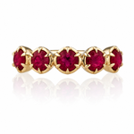 A gold eternity-style ring featuring five round-cut deep red gemstones in a prong setting, shown on a clean white background with a soft reflection below.