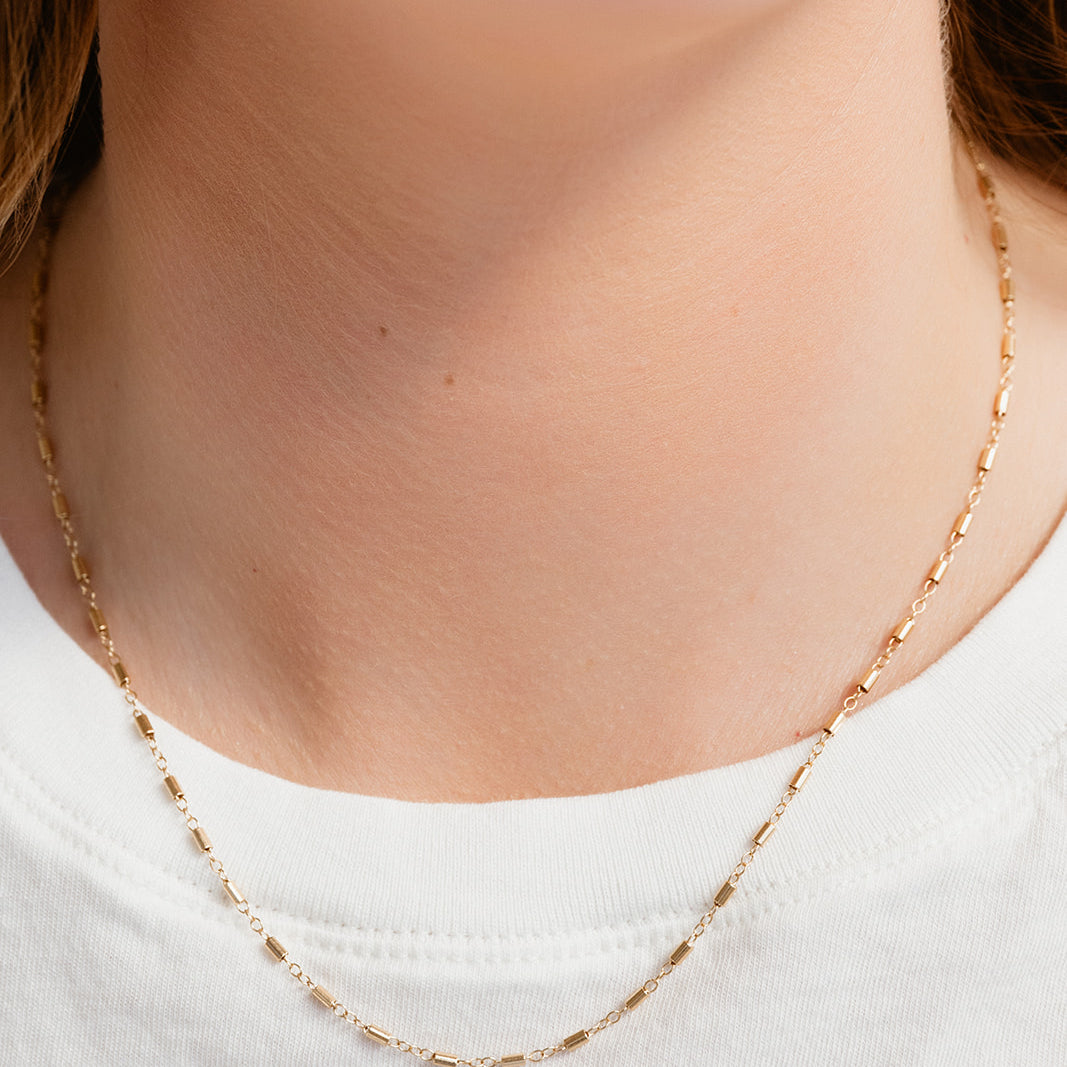 Gold necklace worn by a person on a plain background