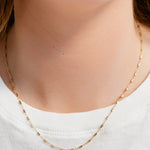 Gold necklace worn by a person on a plain background