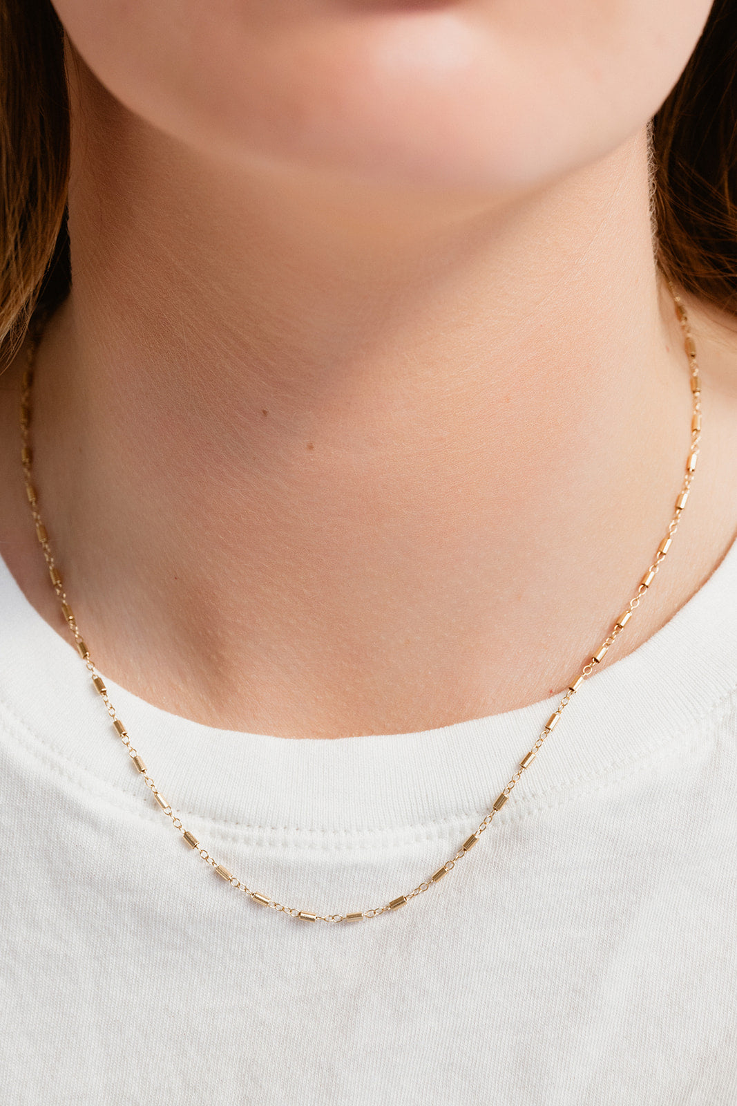 Gold necklace worn by a person on a plain background