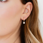 Close-up of a person wearing gold earrings with a diamond drop on a neutral background