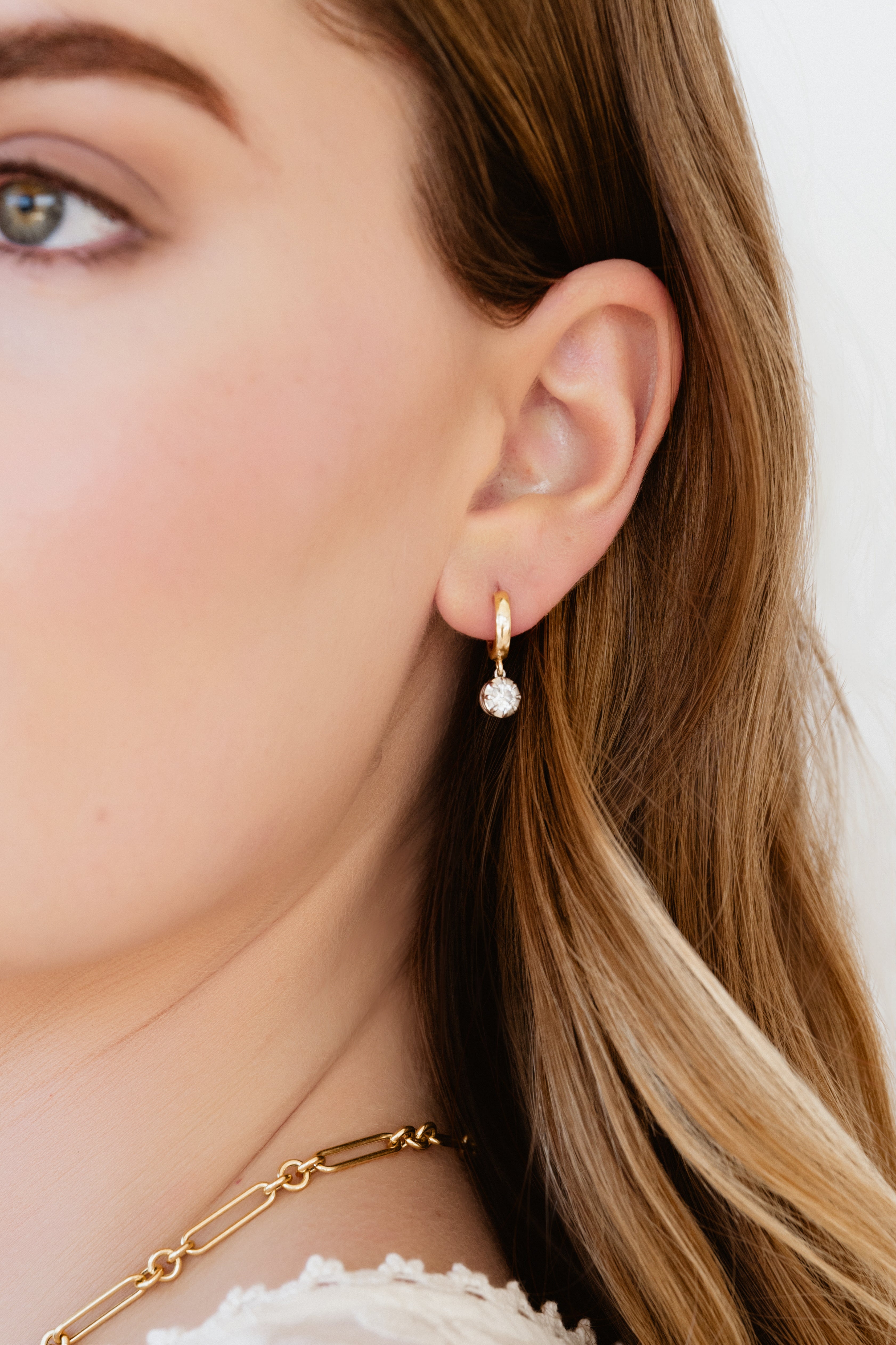 Close-up of a person wearing gold earrings with a diamond drop on a neutral background
