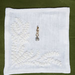 White embroidered fabric square with a pendant on a green background