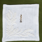 White embroidered fabric square with a pendant on a green background