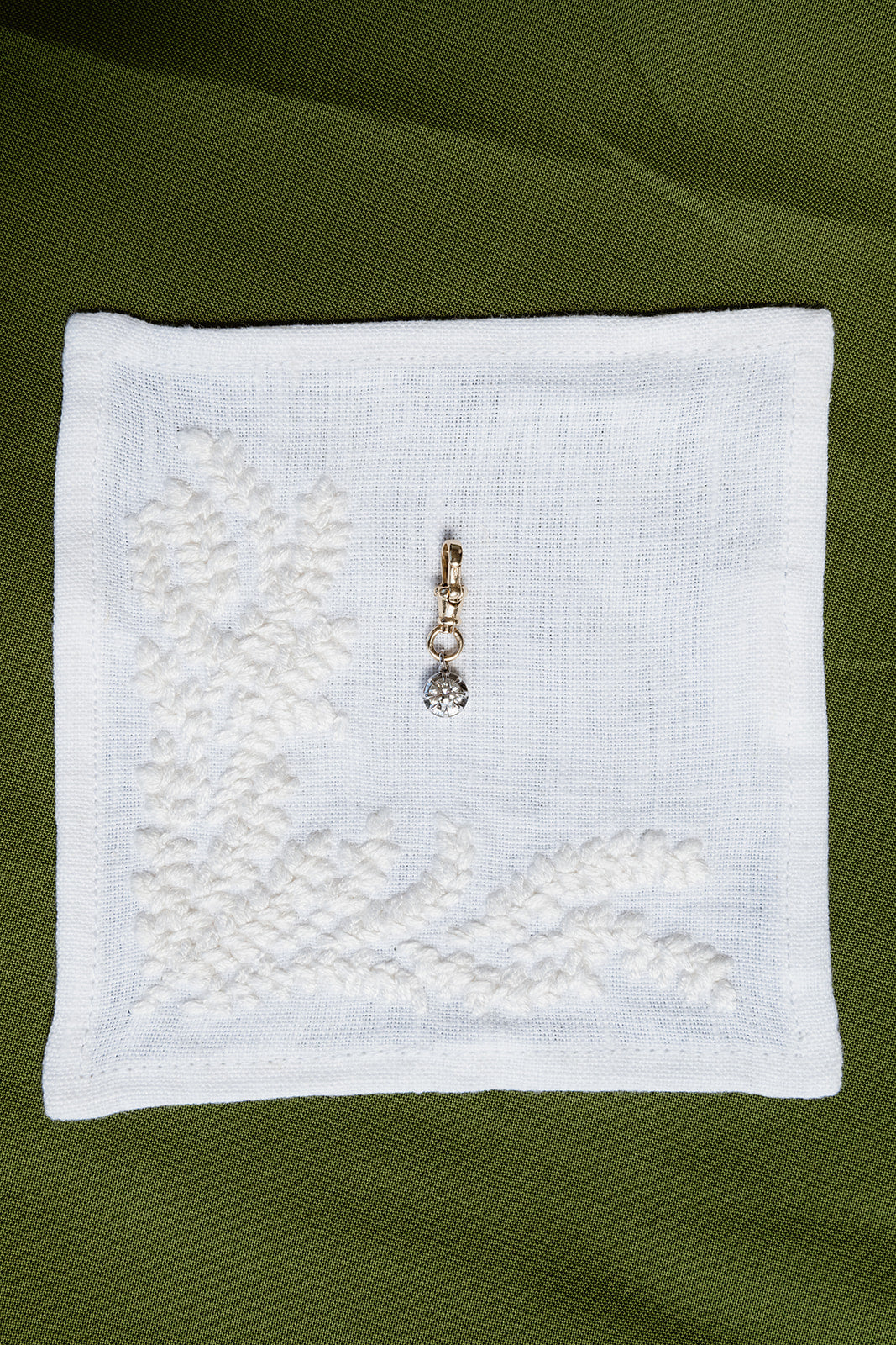 White embroidered fabric square with a pendant on a green background