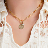 Gold necklace with a pendant on a person wearing a white lace top.