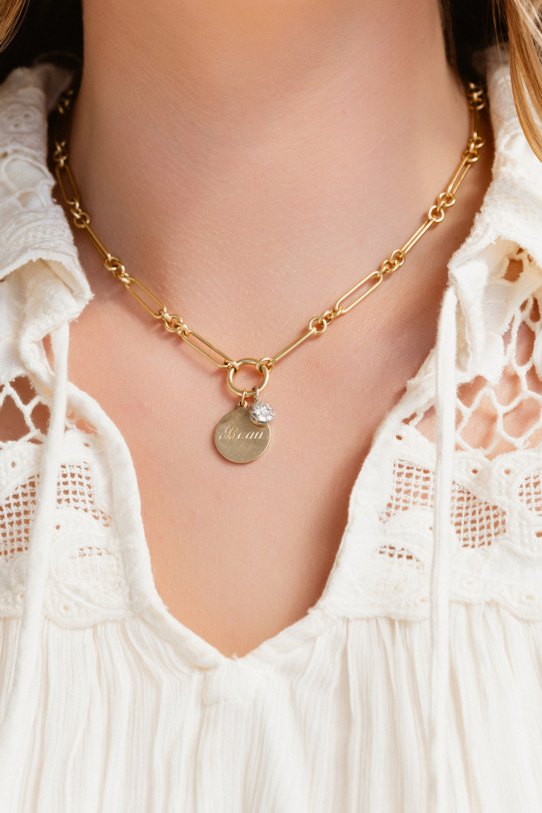 Gold necklace with a pendant on a person wearing a white lace top.