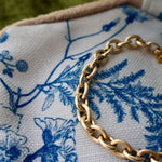 Gold chain bracelet on a blue and white fabric with floral patterns