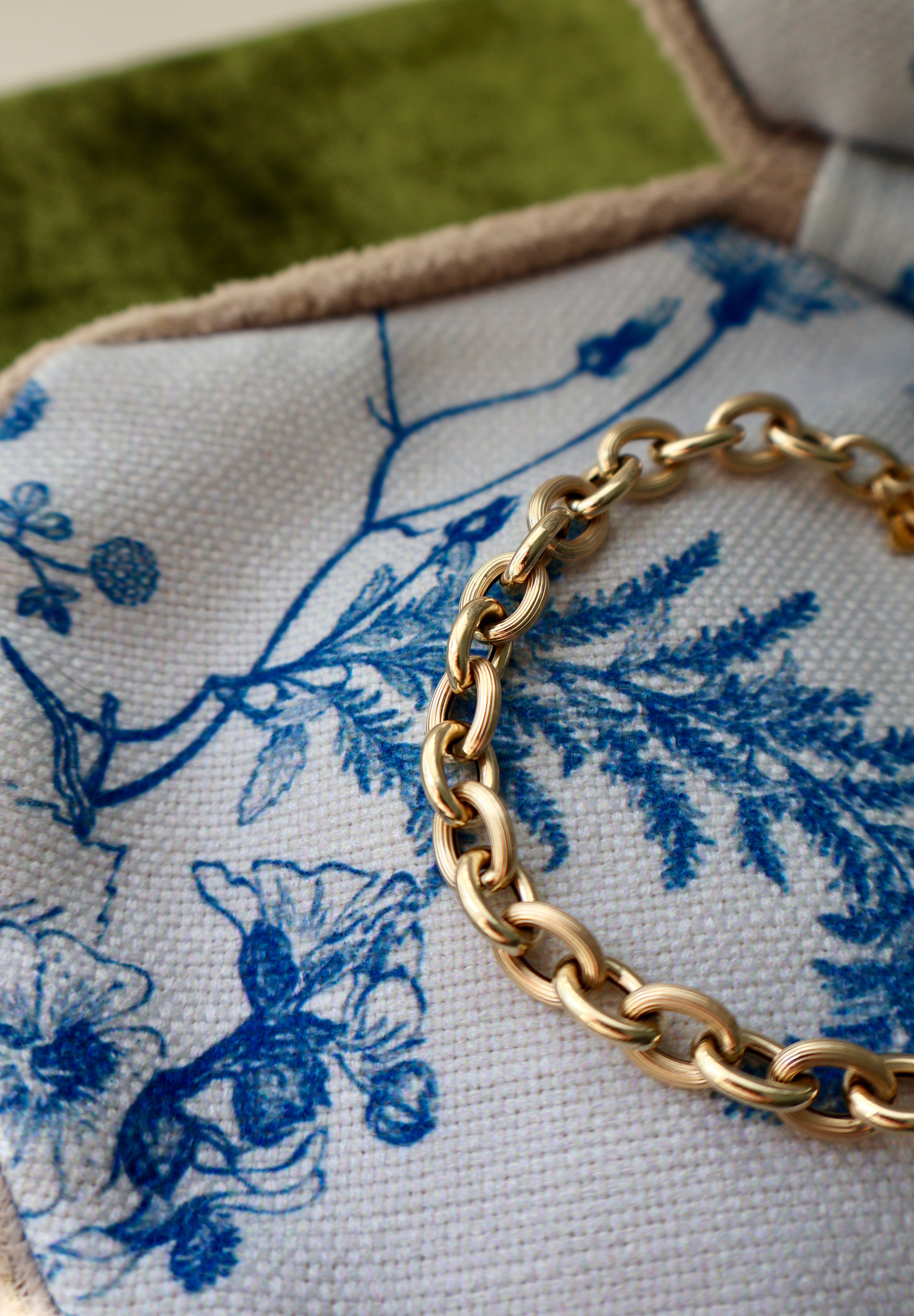 Gold chain bracelet on a blue and white fabric with floral patterns